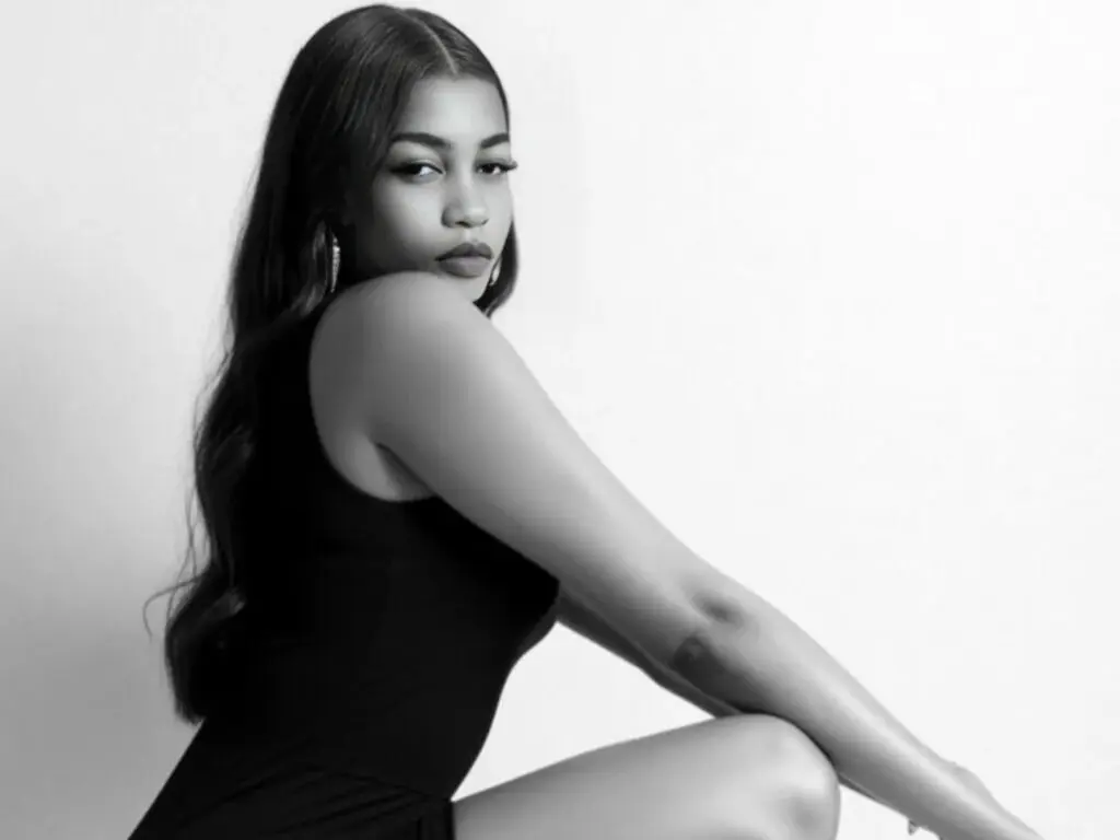 Elegant woman in a black sleeveless top posing against a white background in a moody black and white portrait.