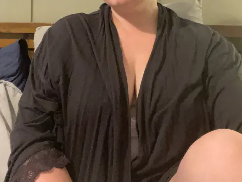 TheaNova — TheaNova wears a black open robe while sitting on a bed.