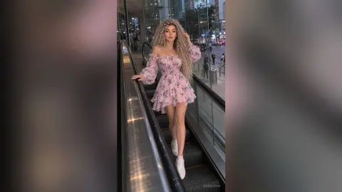 Glamorous woman in a pink floral mini dress posing on an escalator in a modern urban setting.
