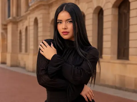 Young woman with long dark hair wearing a black long-sleeve top standing before classic stone architecture.