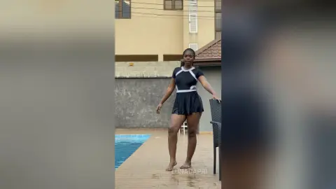 Young woman in a black and white swimsuit standing by a swimming pool on a sunny day.