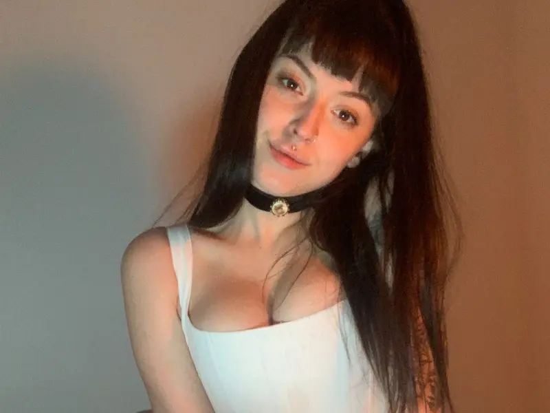 dovesdiary with dark bangs and a nose ring poses in a black lace bra while leaning against a piano.