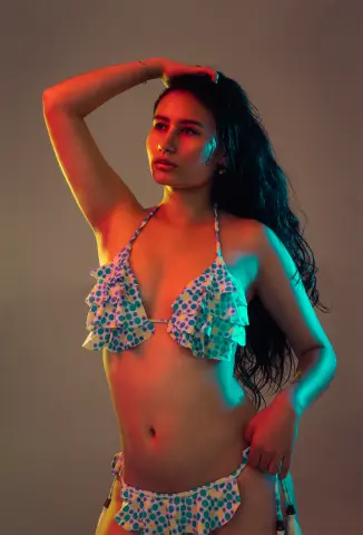 Young woman in a polka dot bikini posing under colorful studio lights with a moody, cinematic aesthetic.