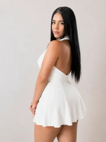 Young woman in a white sleeveless mini dress posing against a neutral studio background with a serene mood.