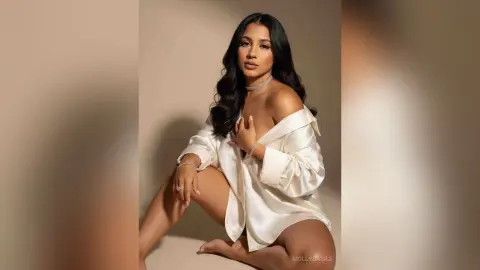 Elegant woman in a white satin shirt and diamond necklace posing against a neutral studio background.