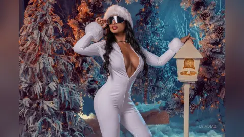 Glamorous woman in a white jumpsuit and faux fur accessories posing in a snowy winter wonderland setting.
