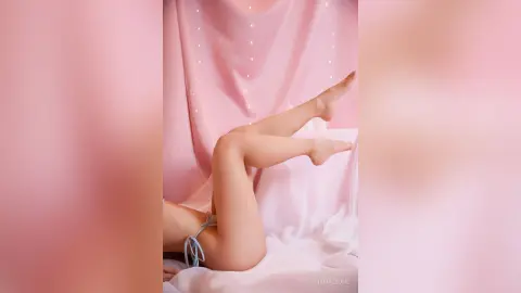 Young woman in light blue bikini relaxing on white bedding in a dreamy pink aesthetic bedroom setting.