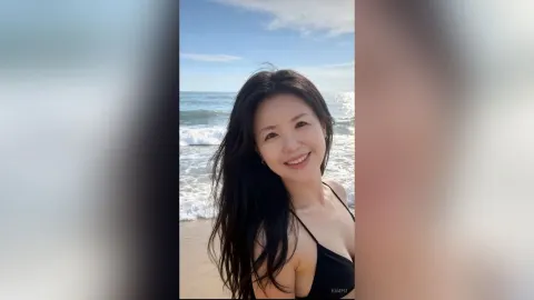KimFu — KimFu smiles at the camera while wearing a black bikini top on a sunny beach.