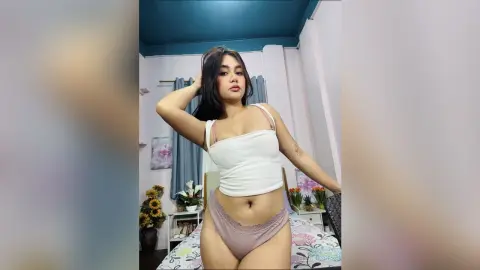 Young woman in a white crop top and mauve briefs posing in a bright bedroom setting.
