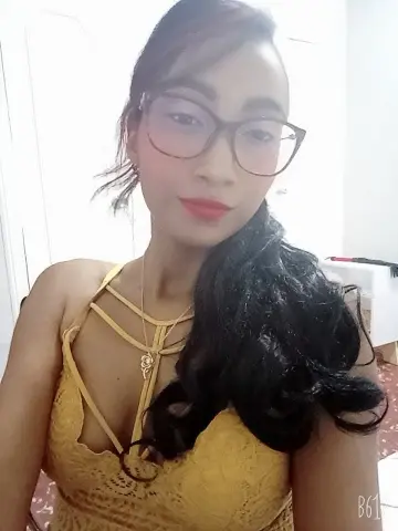 Smiling young woman in a yellow lace sundress and glasses posing indoors for a portrait.
