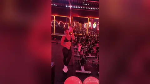 Fit woman in black sports bra and leggings taking a selfie in a moody, red-lit modern gym setting.