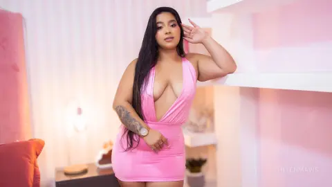 Curvy woman in a pink plunging cocktail dress posing in a bright, modern pink room.