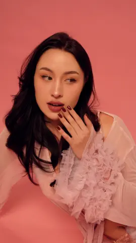 Young woman in a romantic pink ruffled blouse posing against a soft pink background with a dreamy mood.