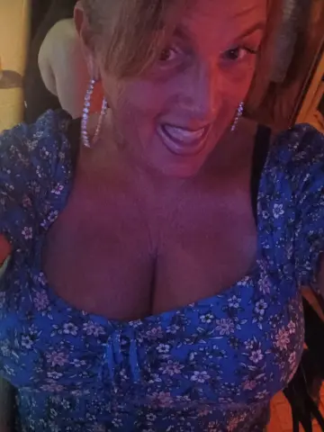 BBWgoDDDess — BBWgoDDDess smiles while wearing a blue floral print top that shows off her cleavage and large breasts.