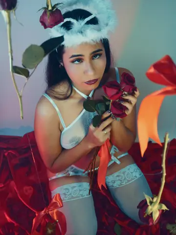 Romantic woman in white lace lingerie and stockings holding red roses in a dreamy, moody setting.