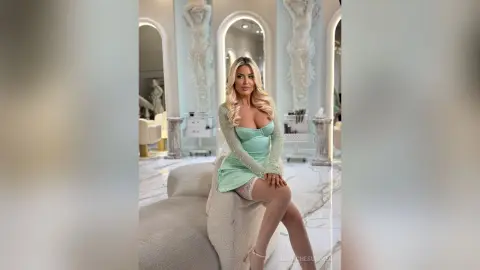 Blonde woman in a mint green sequin cocktail dress posing elegantly in a luxurious marble interior.