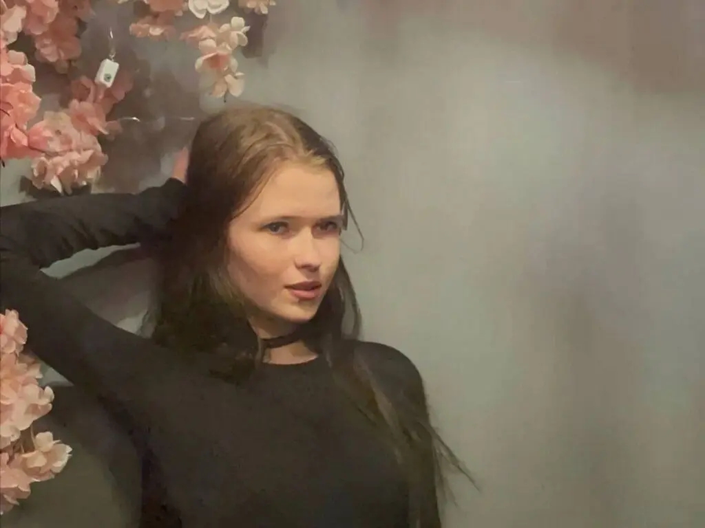 Young woman in a black long-sleeve top posing against a floral background with a moody aesthetic.