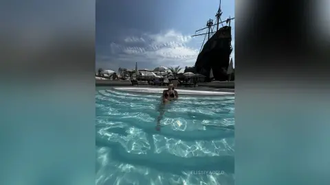 Woman in black bikini relaxing in a luxury resort swimming pool next to a large pirate ship decoration.