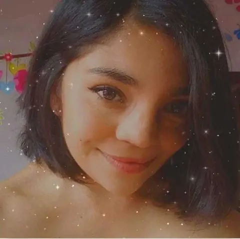 Smiling young woman with short dark hair in a cozy indoor setting with a dreamy, sparkling filter.