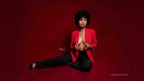 Confident Black woman in a red blazer and black trousers posing against a deep red studio background.