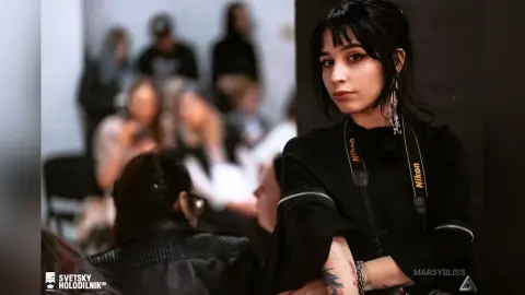 Young woman with dark hair wearing a black Nikon camera strap in a crowded indoor setting.
