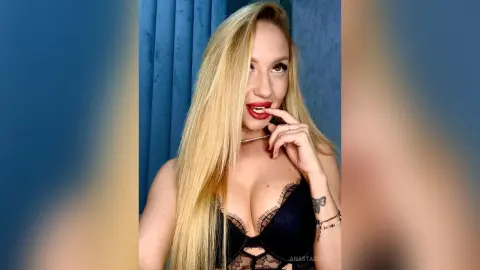 Blonde woman in black lace lingerie posing confidently against a blue background.