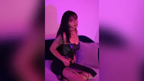Young woman in a black corset top posing in moody pink lighting for a stylish portrait.