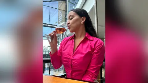 Elegant woman in a bright pink button-down shirt sipping rose wine at an upscale outdoor terrace.