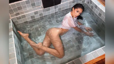 LucyMartin poses naked in a tiled bathtub, her wet skin and hair glistening under the light.