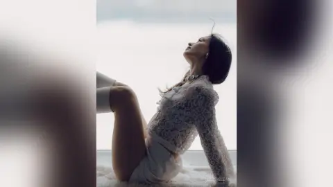 Dreamy portrait of a woman in a white lace top sitting by a window in soft natural light.