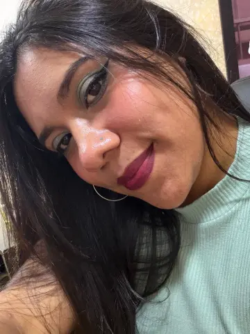 Smiling woman with dark hair and green eyeshadow wearing a light mint ribbed turtleneck top.