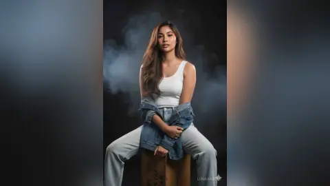 Young woman in white tank top and denim jacket sitting against a moody, smoky dark background.