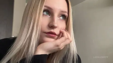 Blonde woman in a black sweater resting her chin on her hand with a thoughtful expression indoors.