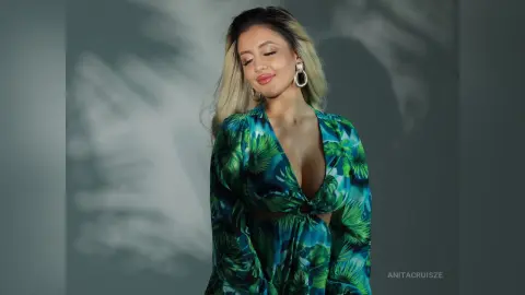 Anita wears a deep-v plunging tropical print blouse with long sleeves and large silver hoop earrings.