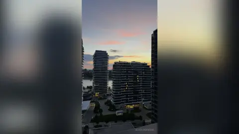 Modern high-rise apartment buildings overlooking a calm river during a colorful sunset twilight.
