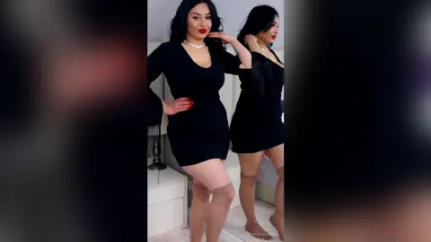 Elegant woman in a black cocktail dress and pearl necklace posing in a bright modern room.