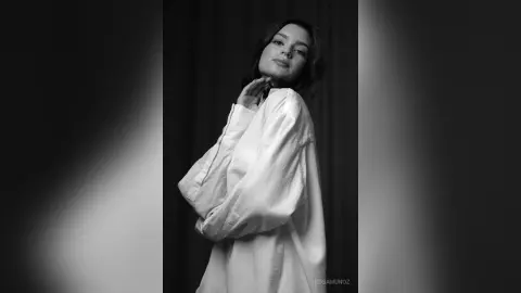 Elegant woman in a white silk blouse posing against a dark backdrop in a moody black and white portrait.
