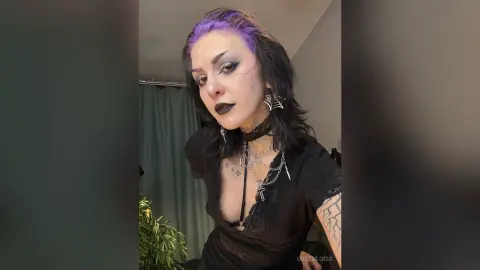 Gothic woman with purple hair and dark makeup wearing black lace outfit and silver jewelry in a moody setting.