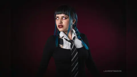 Cosplayer in a black shirt and striped tie with blue hair posing against a dark moody background.