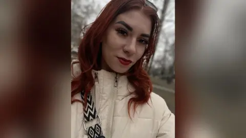 Redheaded woman in a white puffer jacket smiling outdoors in a moody, overcast setting.