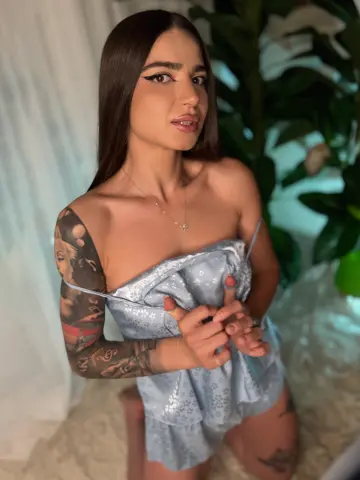 Young woman with long dark hair in a light blue satin slip dress posing in a soft, moody indoor setting.