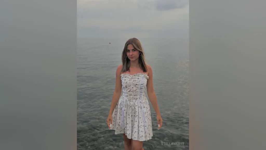 Young woman in a white floral sundress standing by the ocean during a calm sunset.