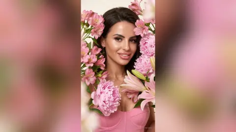Beautiful woman in a pink dress surrounded by blooming pink lilies in a soft, romantic floral setting.