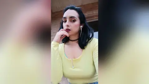 Young woman in a pale yellow long-sleeve top and black choker posing with a thoughtful expression outdoors.