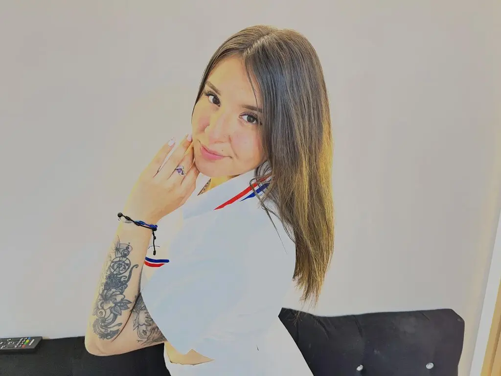 Smiling woman with long brown hair wearing a white shirt in a bright indoor setting.