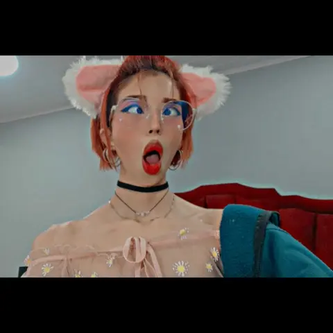 Young woman with cat ears and glasses wearing a floral pink top in a cozy indoor setting.