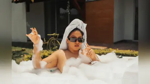 KimRoberth relaxes in a bubble bath wearing a white towel wrap on her head and dark sunglasses.
