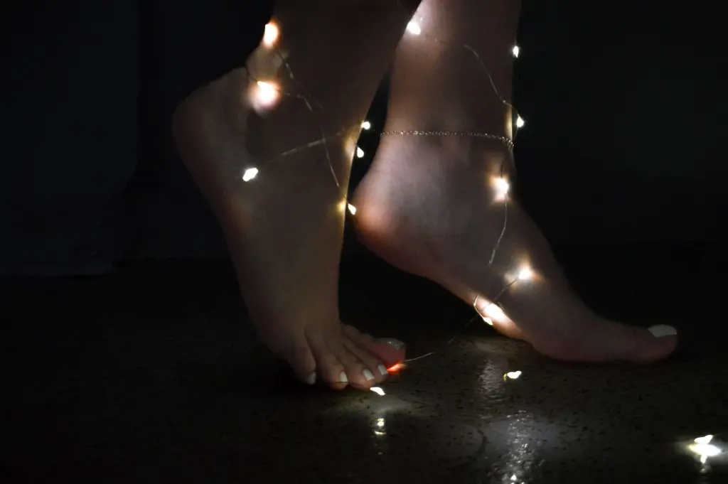 NatachaDiaz111 — Bare feet wrapped in glowing fairy lights on a dark floor creating a magical and cozy nighttime mood.