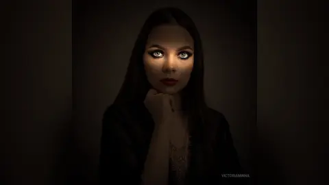 Moody portrait of a woman with dark hair and red lips wearing a black outfit in dim lighting.