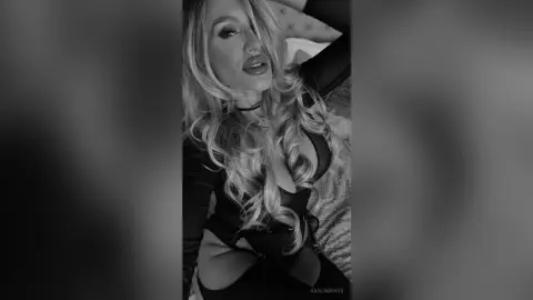 Blonde woman in a black long-sleeve top relaxing in a moody, black and white indoor setting.